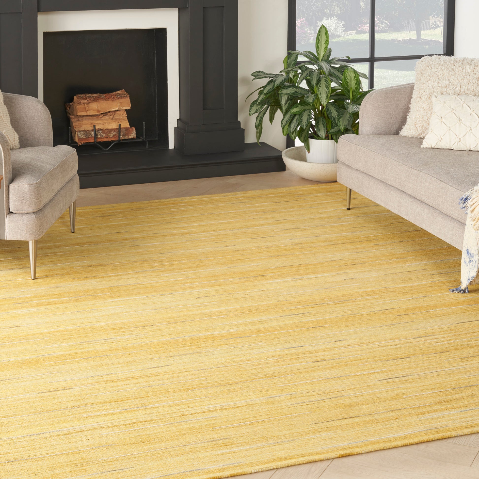 Yellow woven area rug with subtle stripes in a modern living room with gray sofa, fireplace, & plants.