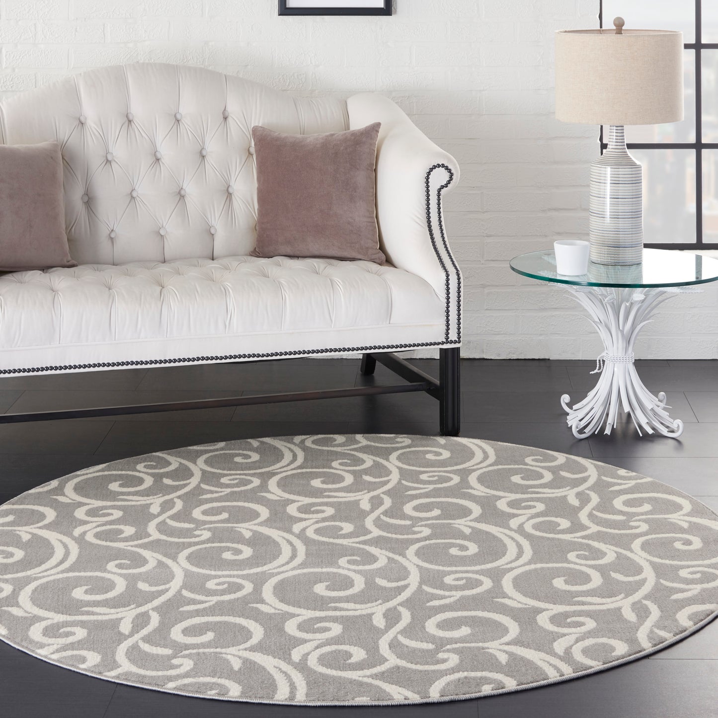 Round grey and white swirl area rug beside a tufted white sofa with taupe cushions and a glass-top side table.