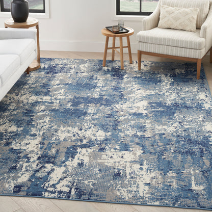 Blue abstract area rug with beige undertones in a bright living room; white sofa, beige armchair & wooden side tables.