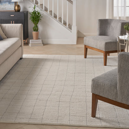 Neutral living room with gray woven rug, gray fabric armchairs on wooden legs, beige sofa, white staircase and green plant.