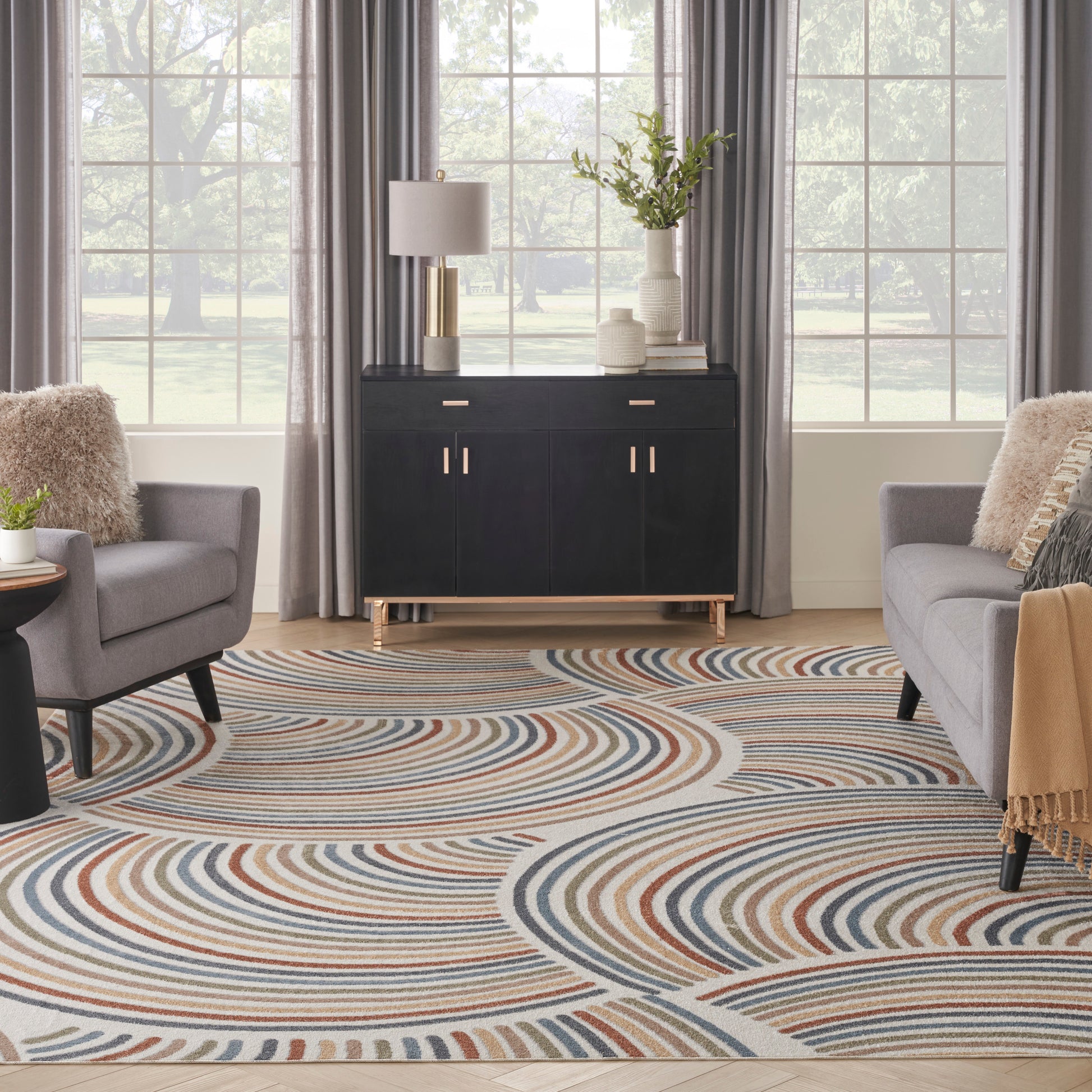 Contemporary living room with circular multicolor swirl rug, black sideboard, gray upholstered armchairs, and beige throws.