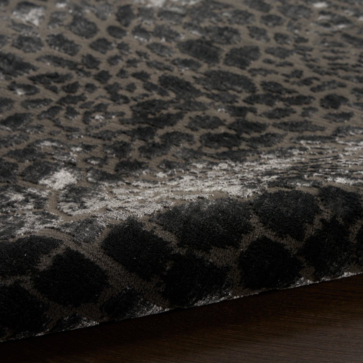 Close-up of a plush leopard print rug in dark gray and black tones with a thick pile, laid over dark wood floor.