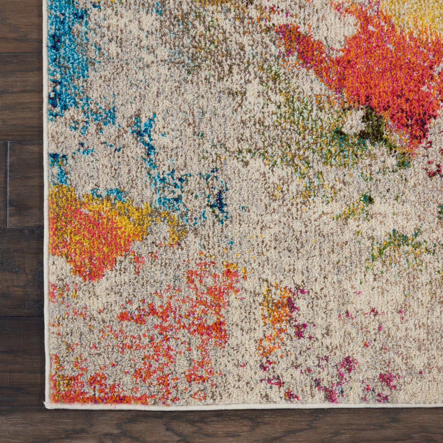 Abstract beige shag rug with colorful splashes in blue, teal, yellow, pink; rectangular, low-pile, on wood floor.