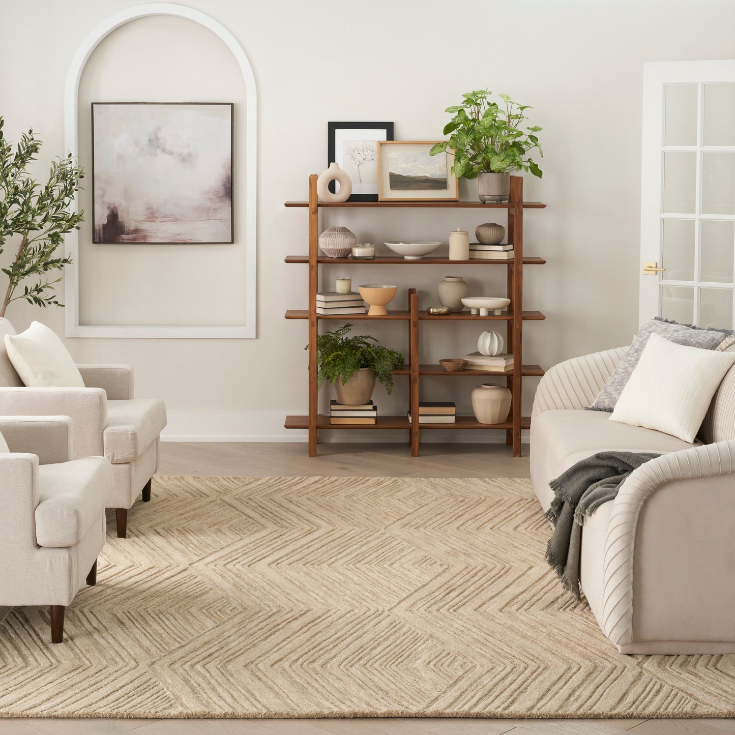 Mid-century wooden bookcase with plants and ceramics in a neutral living room; beige sofa and chairs, abstract art, rug.