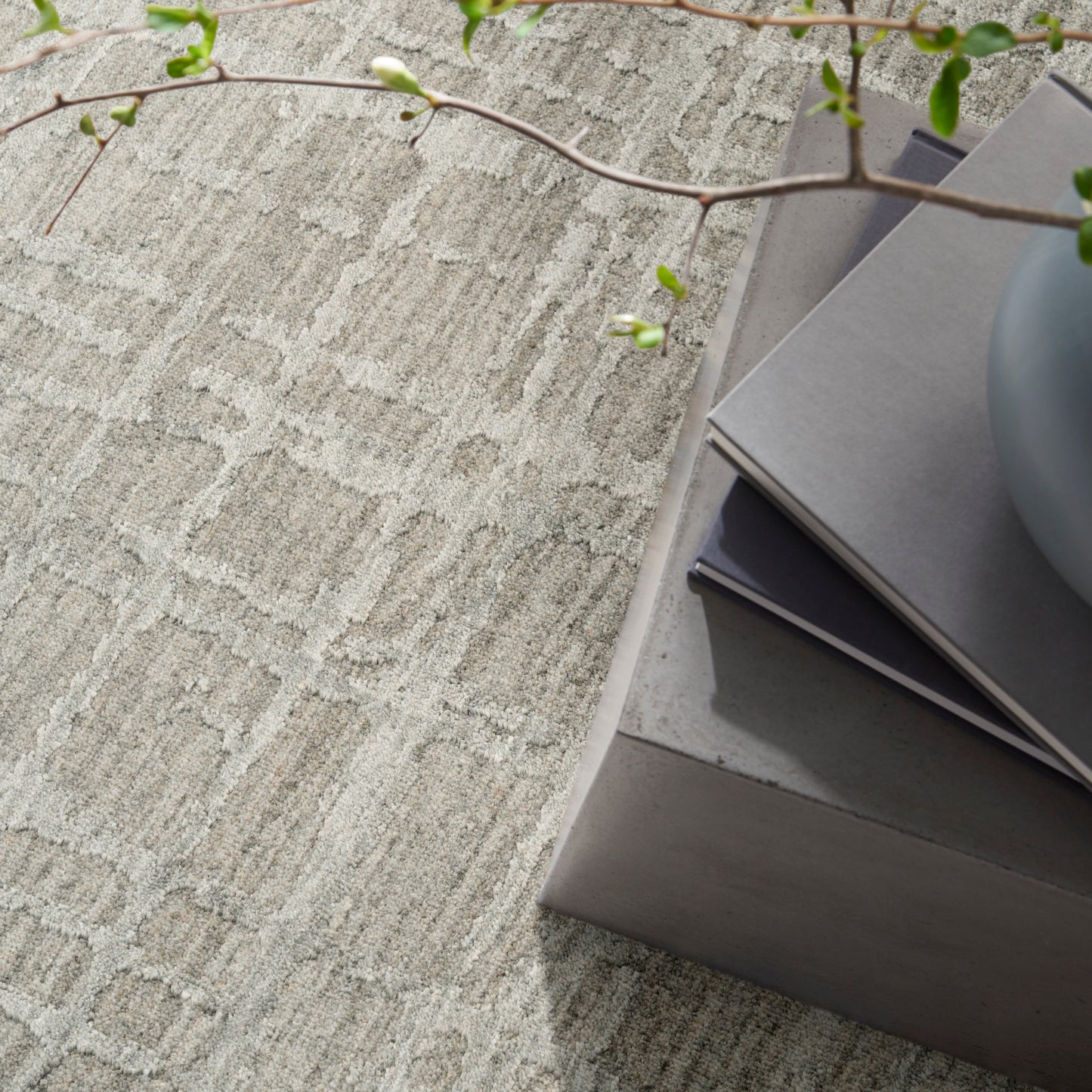 Neutral textured rug with a stack of gray color swatches on a concrete coffee table, a gray vase & a leafy branch.