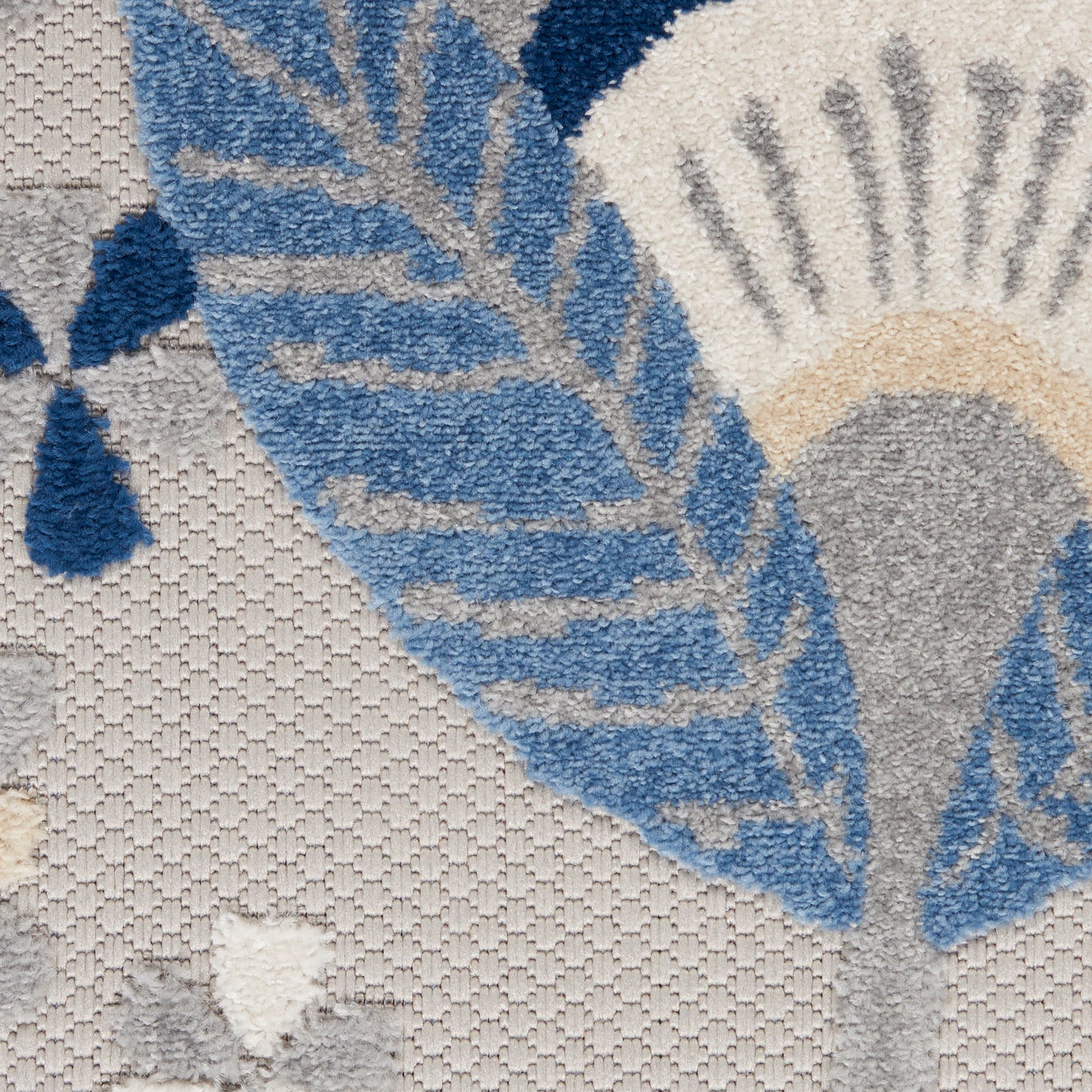 Close-up of a textured area rug featuring blue leaf motifs on a beige background; soft shaggy pile with woven sections.