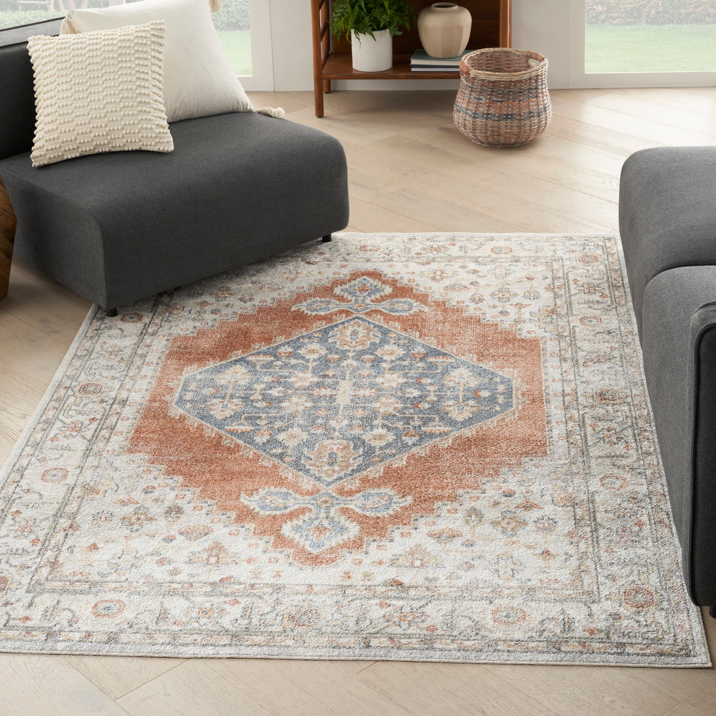 Rectangular oriental rug with orange central diamond, blue-gray motifs on cream field and beige border in a living room.