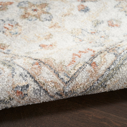 Close-up of a beige patterned rug with pastel blue, peach and gray motifs on a dark wood floor.