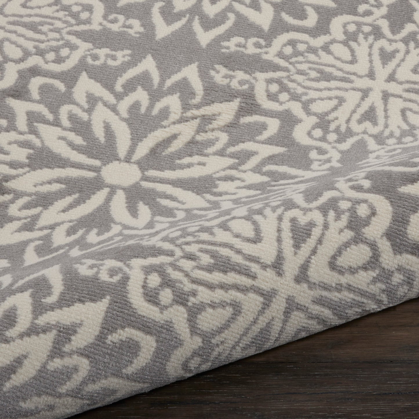 Grey fabric with white damask floral pattern; woven texture, decorative rug/throw on wood surface.