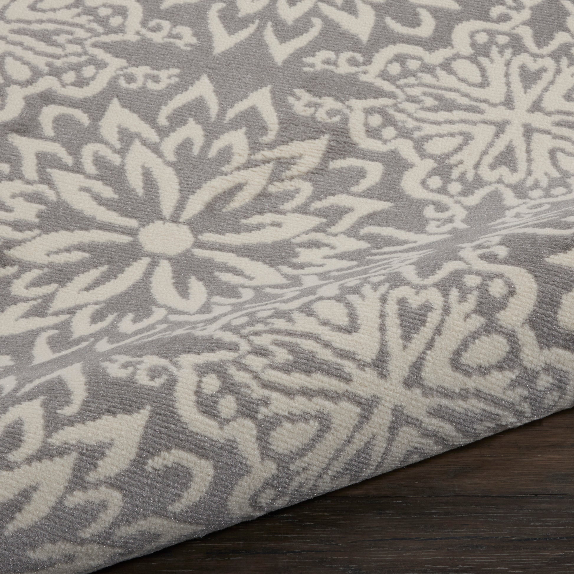 Grey fabric with white damask floral pattern; woven texture, decorative rug/throw on wood surface.