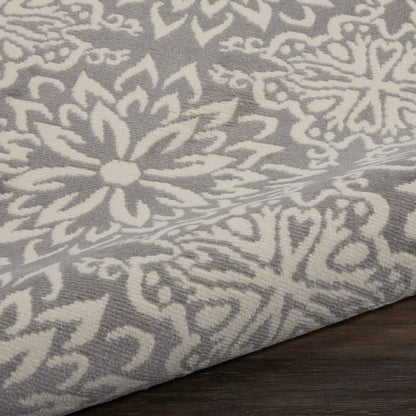 Grey fabric with white damask floral pattern; woven texture, decorative rug/throw on wood surface.