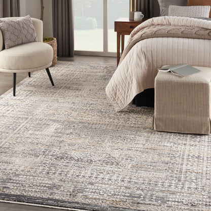 Neutral-toned bedroom with a vintage beige rug, quilted bedspread, knit throw, beige ottoman, and boucle chair.