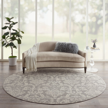Beige curved sofa on round gray patterned rug with fluffy gray cushion, throw blanket in bright modern living room.