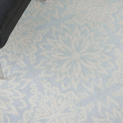 Light blue rug with large white snowflake/mandala pattern; soft textured surface with a partial black chair leg in the corner.