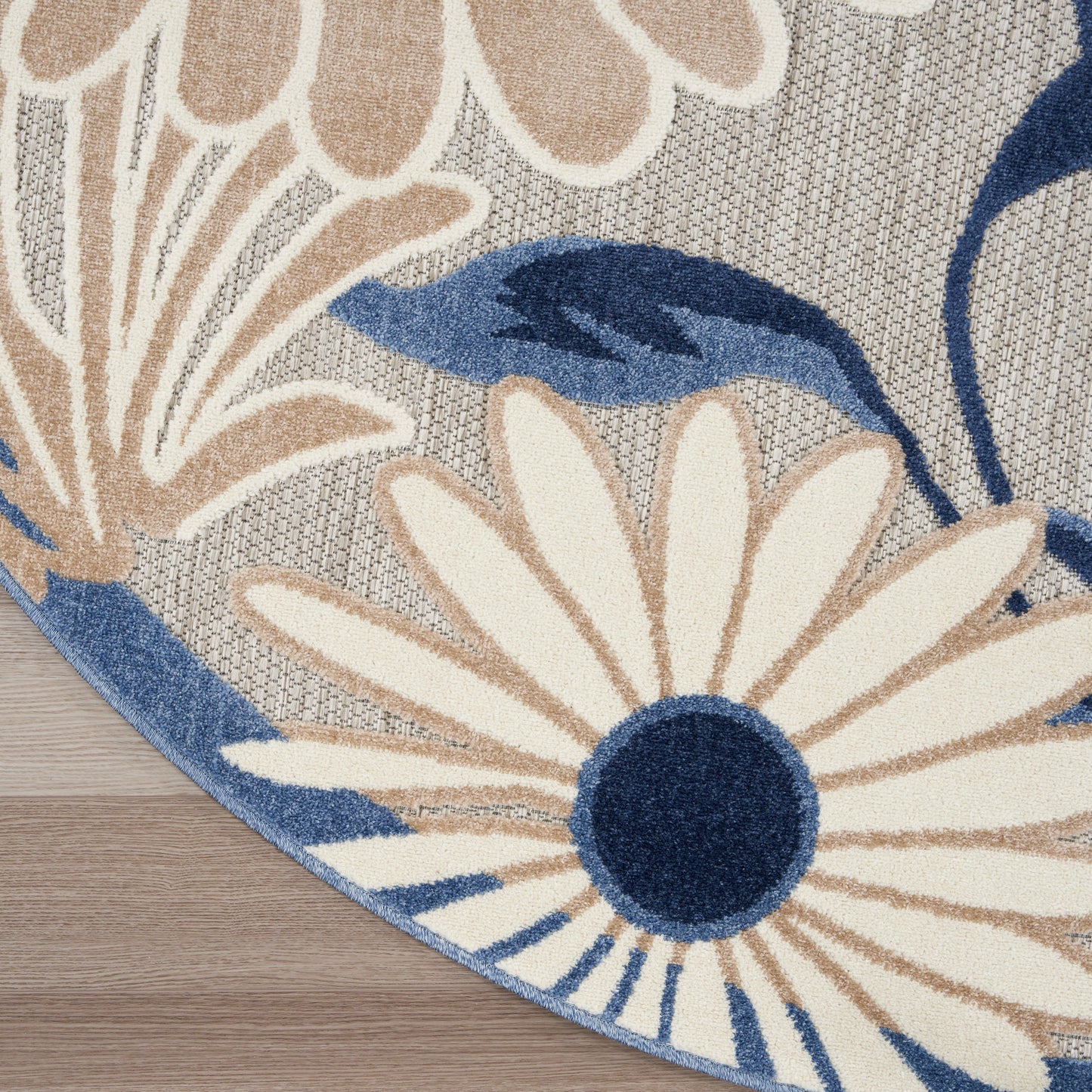 Round area rug with large cream petals, navy centers and blue leaves on a gray woven background.