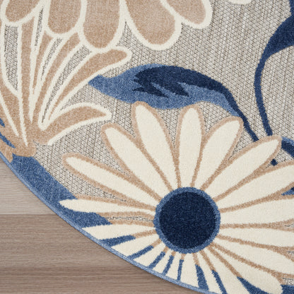 Round area rug with large cream petals, navy centers and blue leaves on a gray woven background.