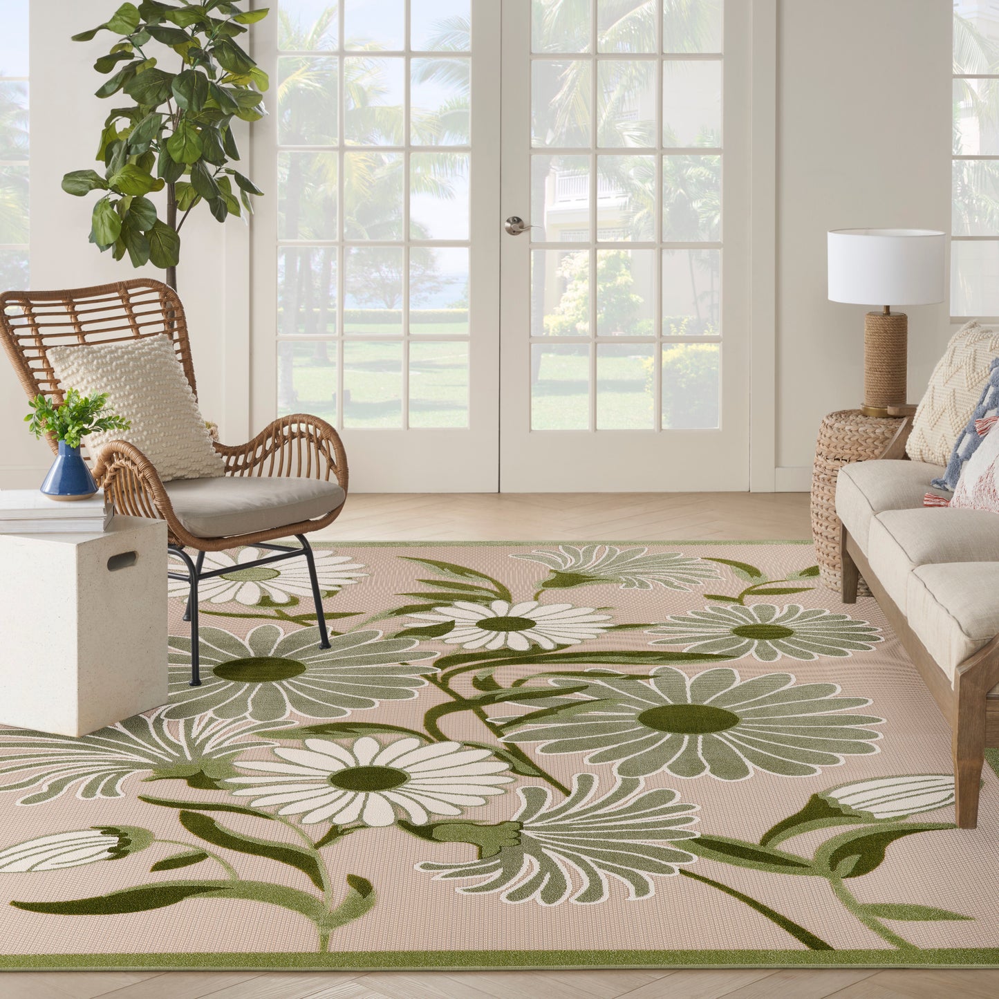 Bright outdoor living area with a beige floral rug featuring white daisies and green vines, wicker chairs, a sofa, and glass doors.