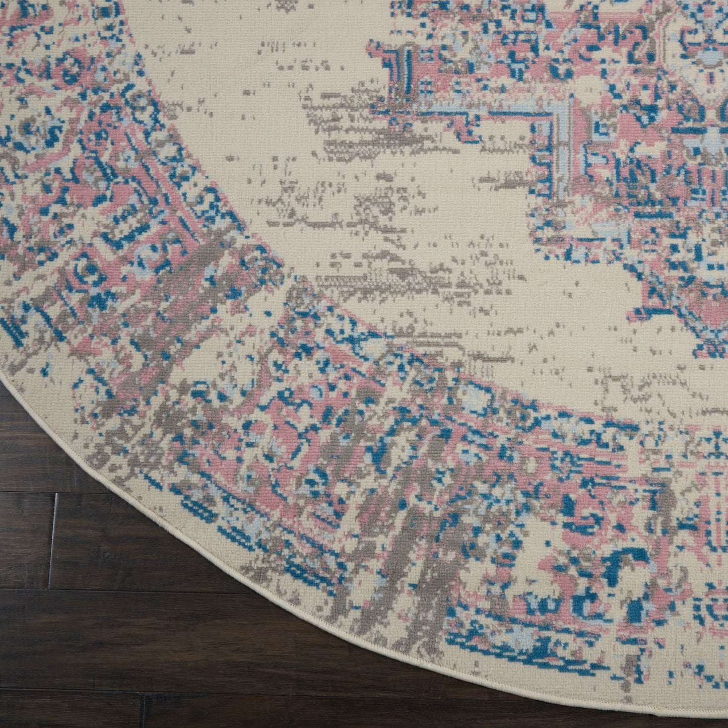 Round rug with distressed Persian-inspired pattern in pink, blue, taupe on beige, placed on dark wood floor.