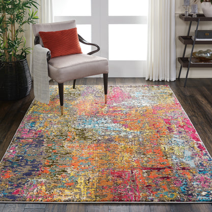 Multicolor abstract area rug on dark hardwood floor beside a beige upholstered armchair with a red throw pillow.