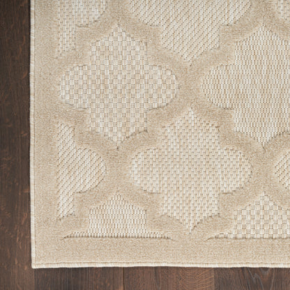 Beige textured area rug with a large quatrefoil lattice pattern on dark wood floor.