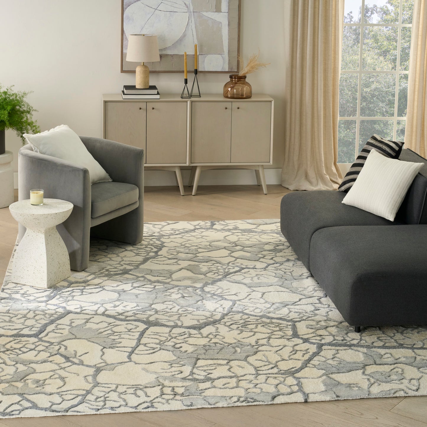 Modern living room with gray upholstered armchairs, pale wood sideboard, speckled white side table, stone-pattern rug, beige curtains.