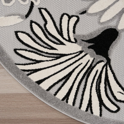 Round gray rug with bold black and cream floral petal motif, woven texture, gray edge, on wooden floor.