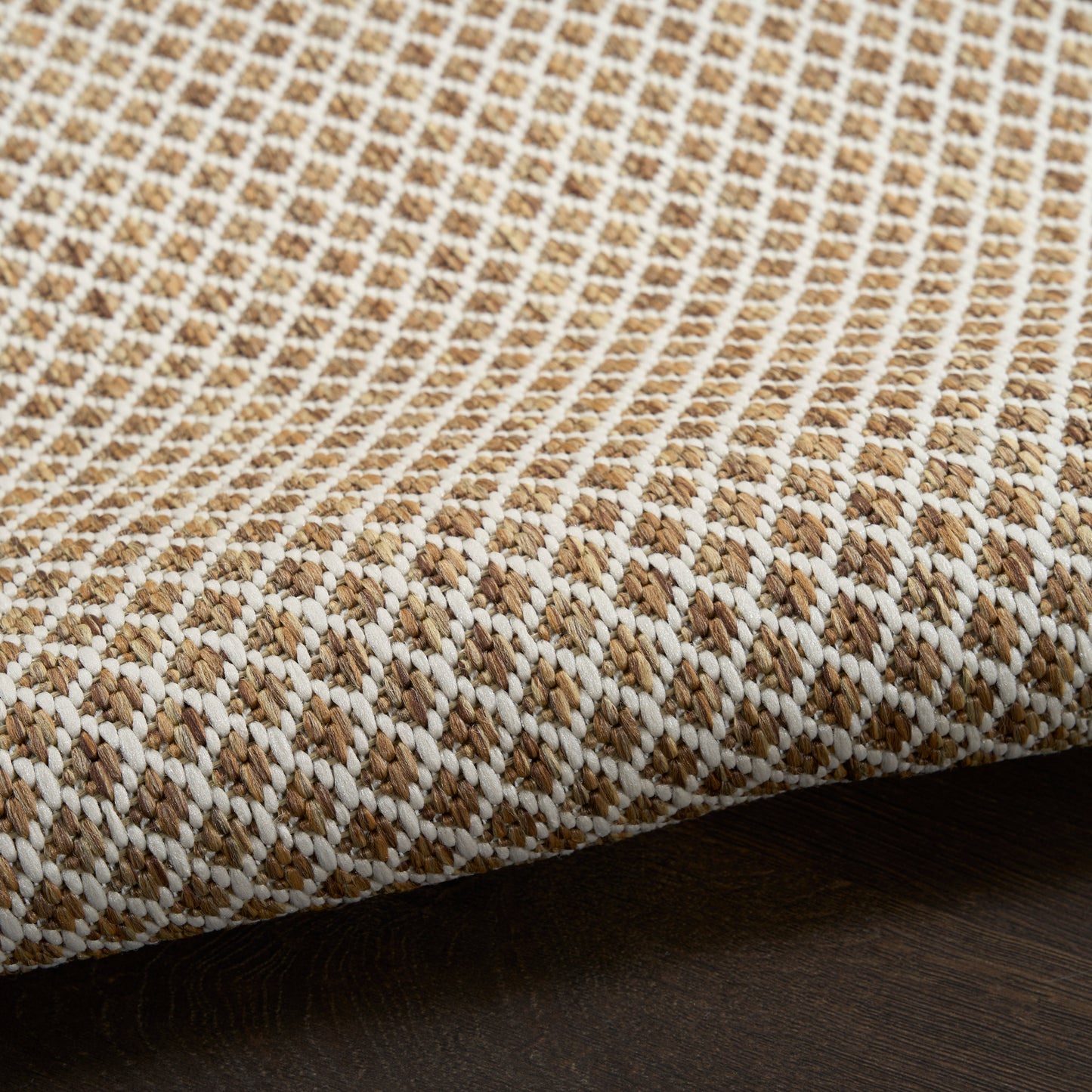 Beige and white woven textile rug with a tight diagonal pattern and folded edge on dark wood surface.