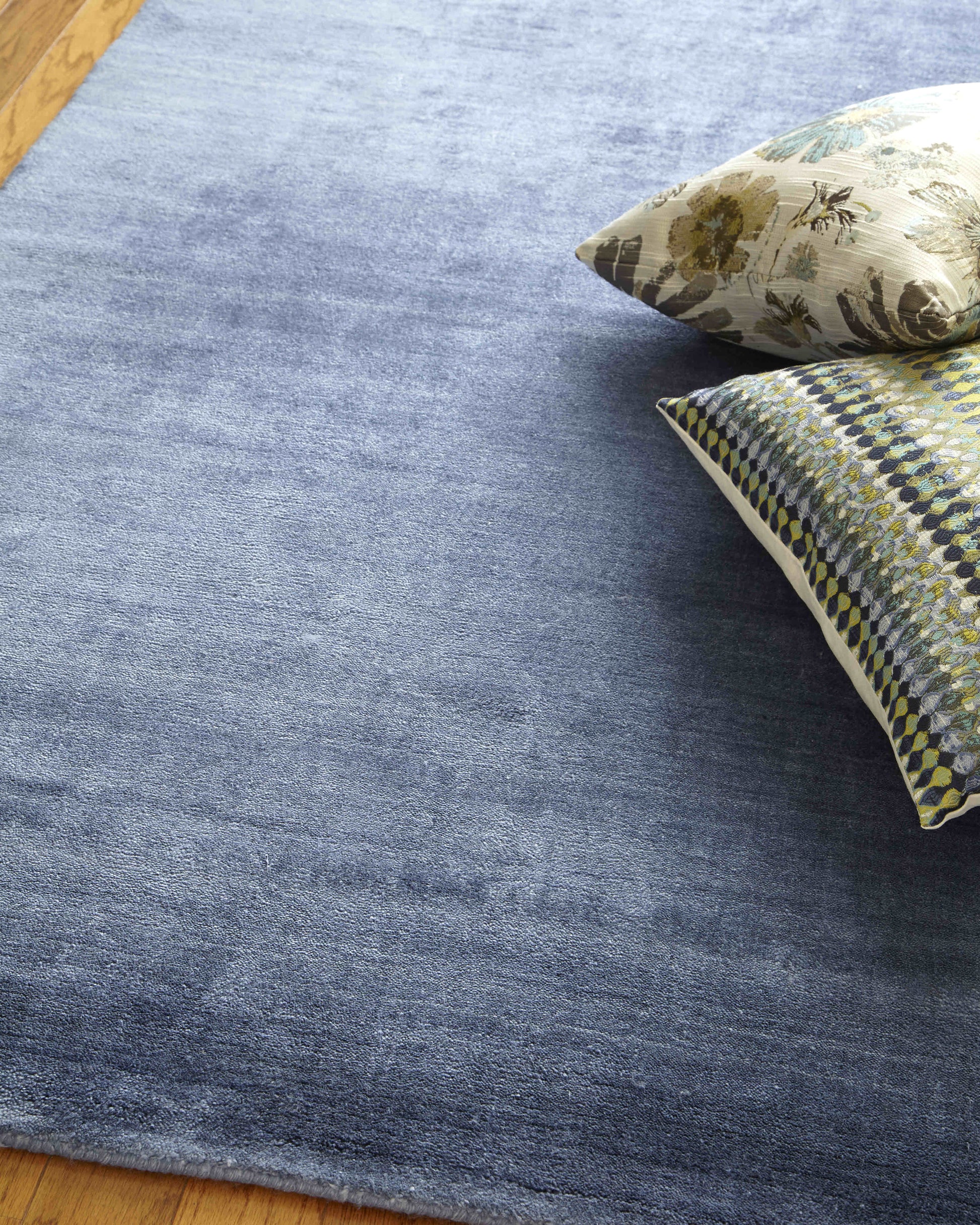 Blue gradient rug on wooden floor with two decorative throw pillows (floral beige and blue-yellow geometric).