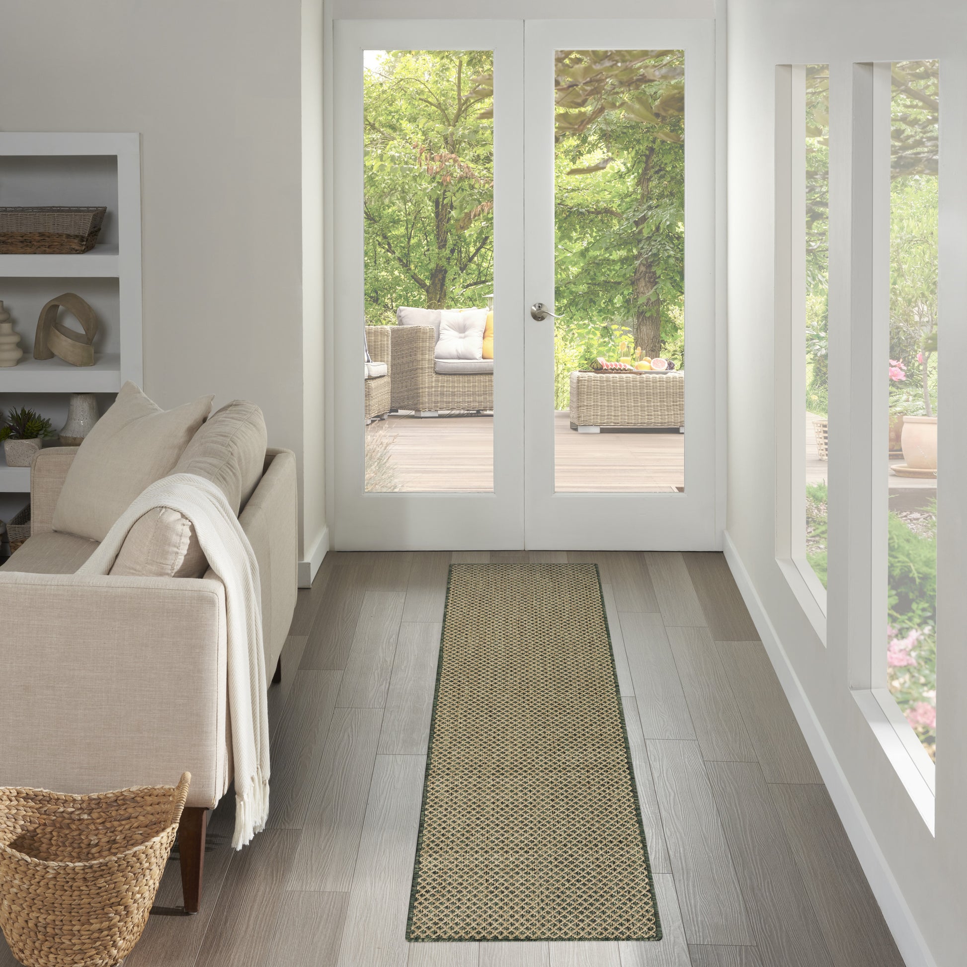 Bright living room with a beige sofa, light wood floors, a long woven runner rug, and French doors to a garden patio.