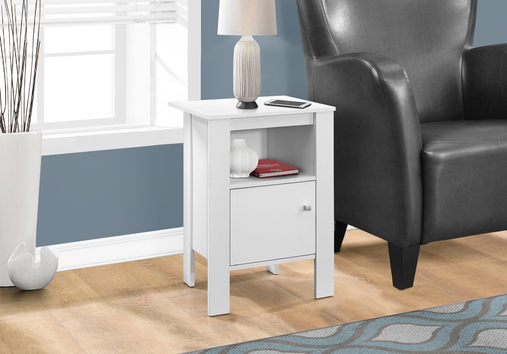 White wood end table with shelf, lamp on top & red book, beside a gray leather armchair.