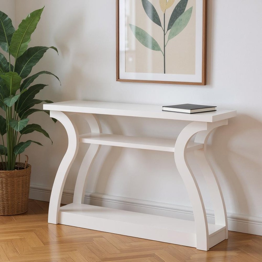 White console table with curved arch legs and lower shelf, black book on top, framed botanical art on wall.