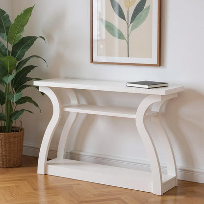 White console table with curved arch legs and lower shelf, black book on top, framed botanical art on wall.