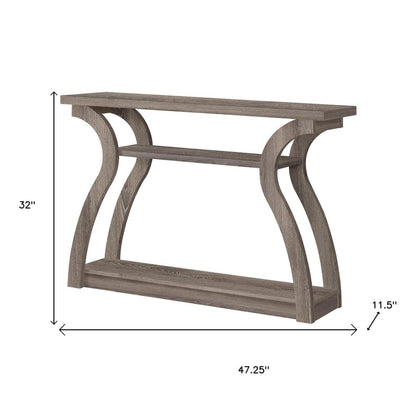Taupe-toned wood console table with curved trestle legs and a lower shelf.