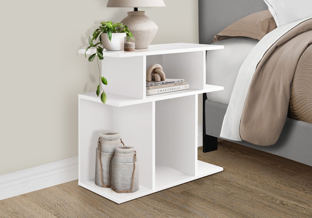 White open-shelf nightstand beside a bed; top lamp and plant, books on middle shelf, fabric jars in lower cubby.