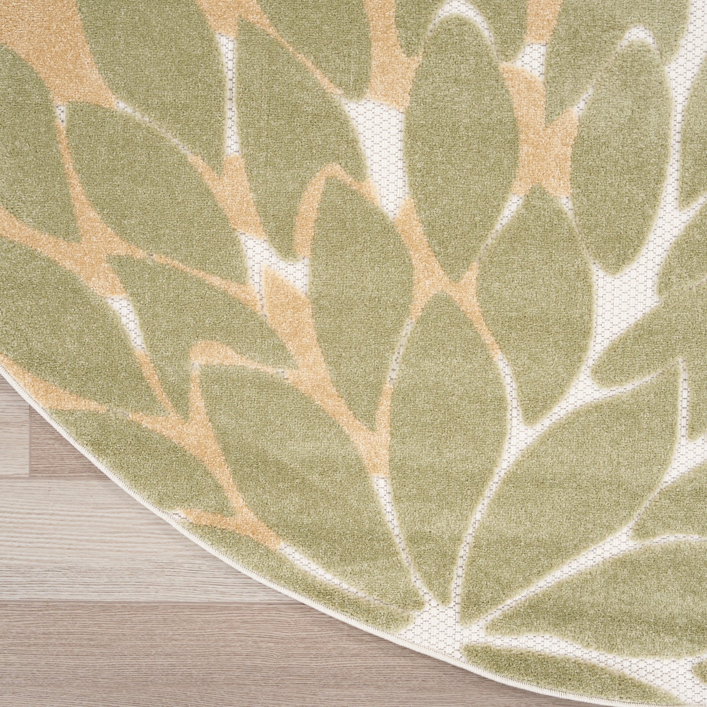 Round outdoor rug with olive-green leaf pattern on beige background, resting on light wood floor