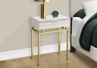 Whitewashed nightstand with a single drawer and gold metal legs; gold lamp and round clock on top in a bedroom scene.