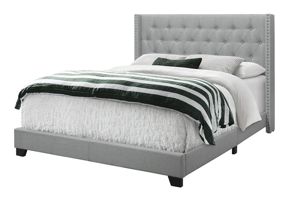 Gray upholstered bed with tufted headboard and nailhead trim, low platform; white bedding with green-striped throw.