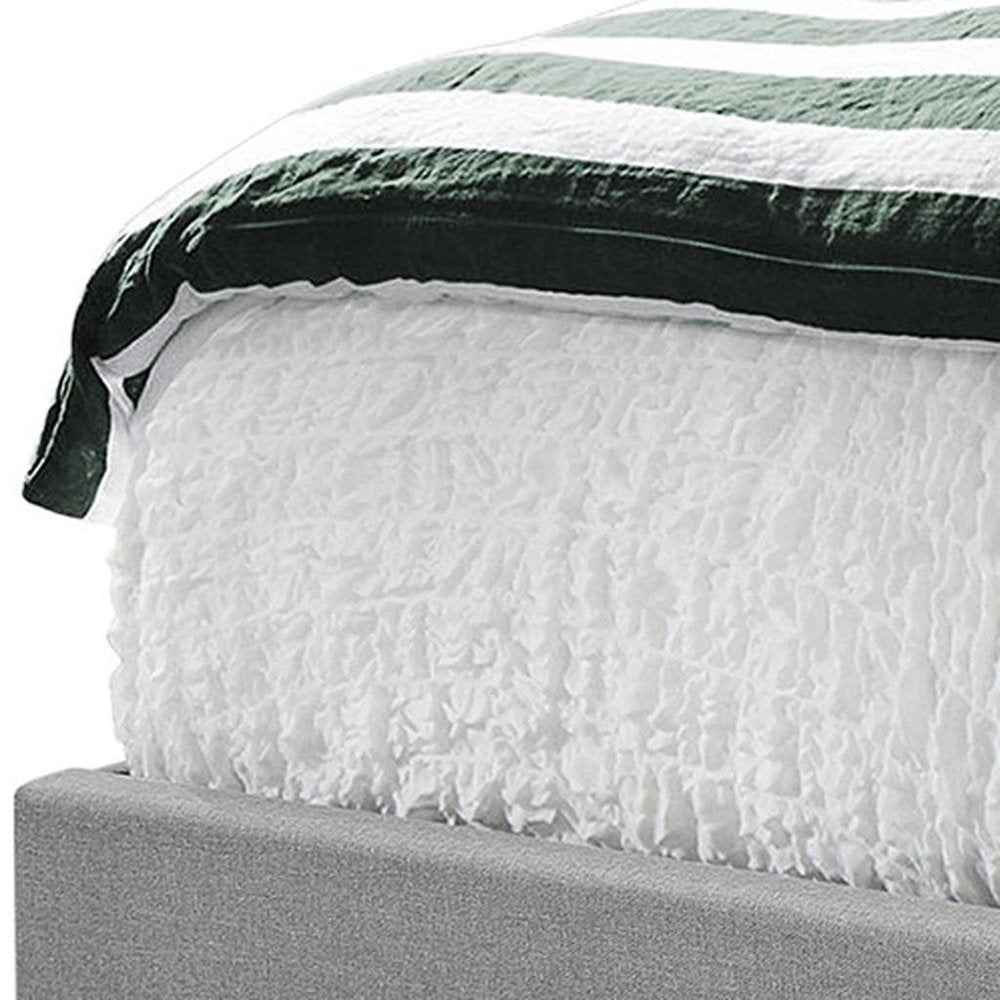 Gray upholstered bed frame with white ruched comforter and dark green striped throw blanket.