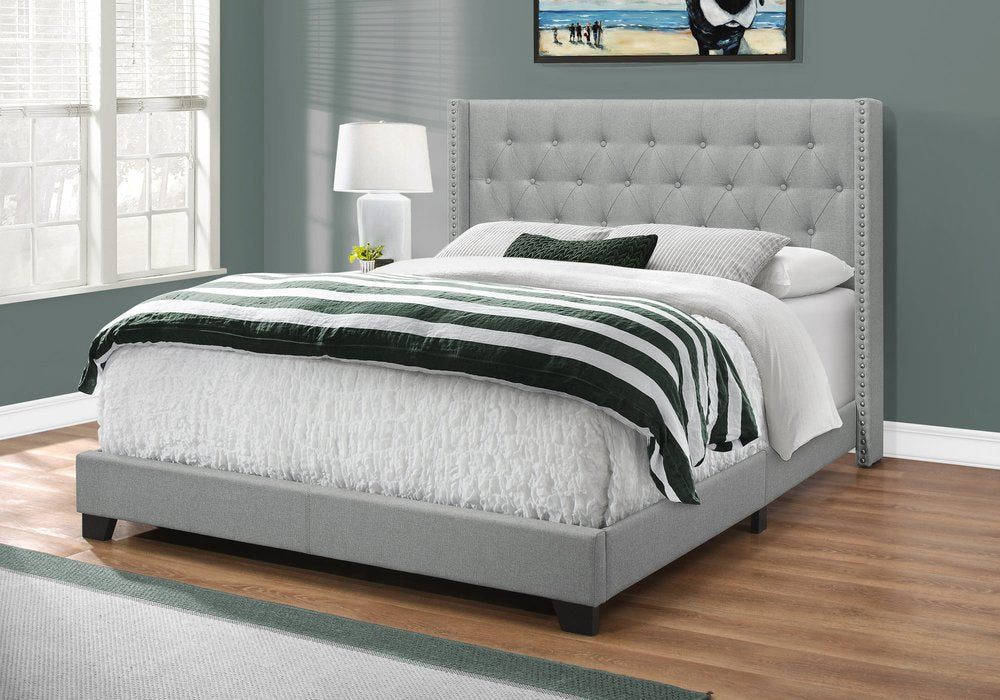 Grey tufted platform bed with nailhead trim, white bedding and black-white striped throw in a teal-walled bedroom.