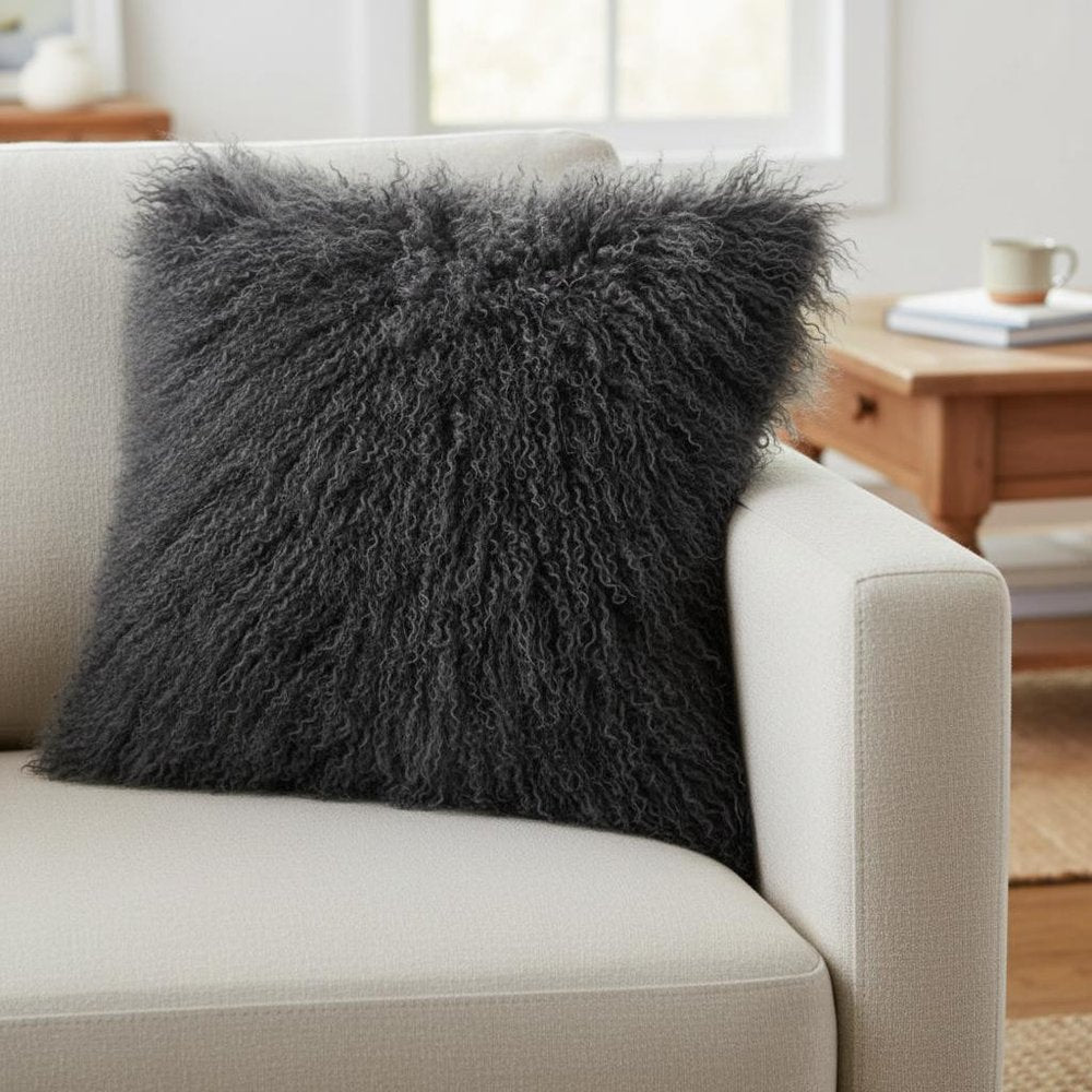 24" charcoal gray genuine Tibetan lamb fur pillow with microsuede backing on a beige sofa, a cozy modern living room accent.