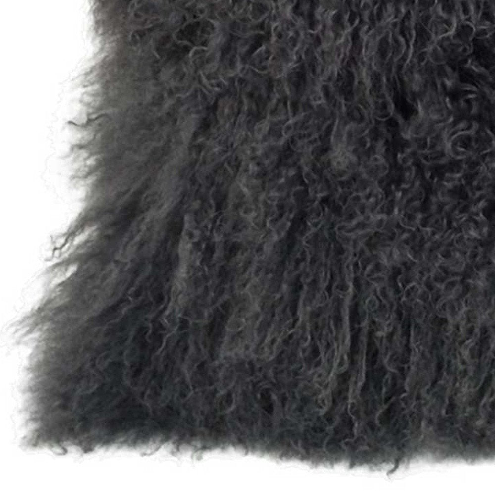 Close-up of charcoal Tibetan lamb fur on a pillow with microsuede backing; long curly pile, soft and plush.