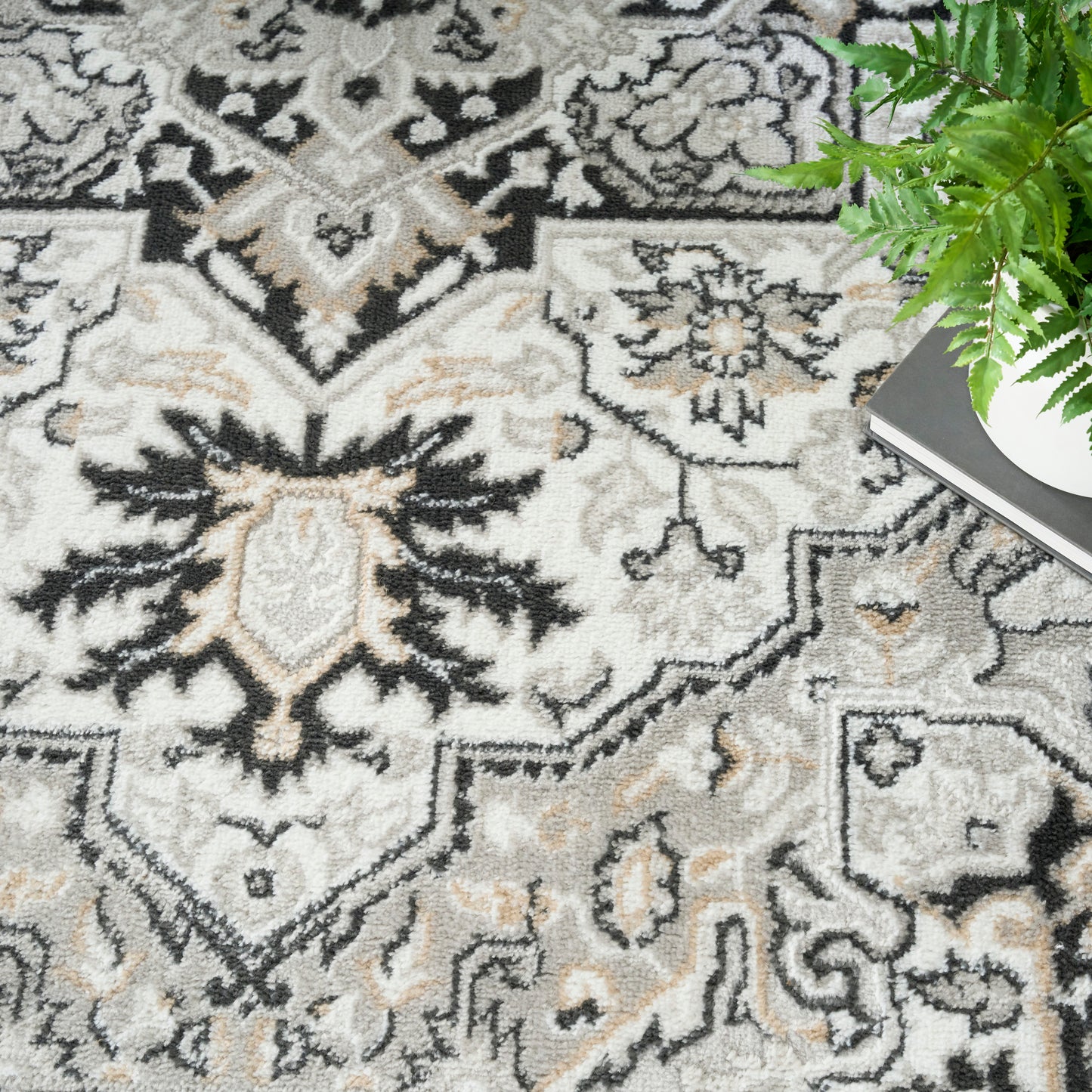Soft textured oriental rug in beige, gray and black with floral medallions; plant and book nearby.