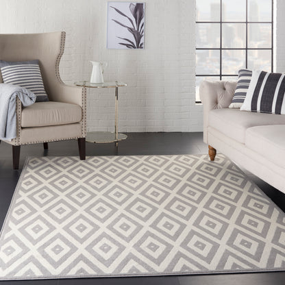 Light gray geometric rug in a contemporary living room with beige armchairs, striped cushions, and a glass side table.