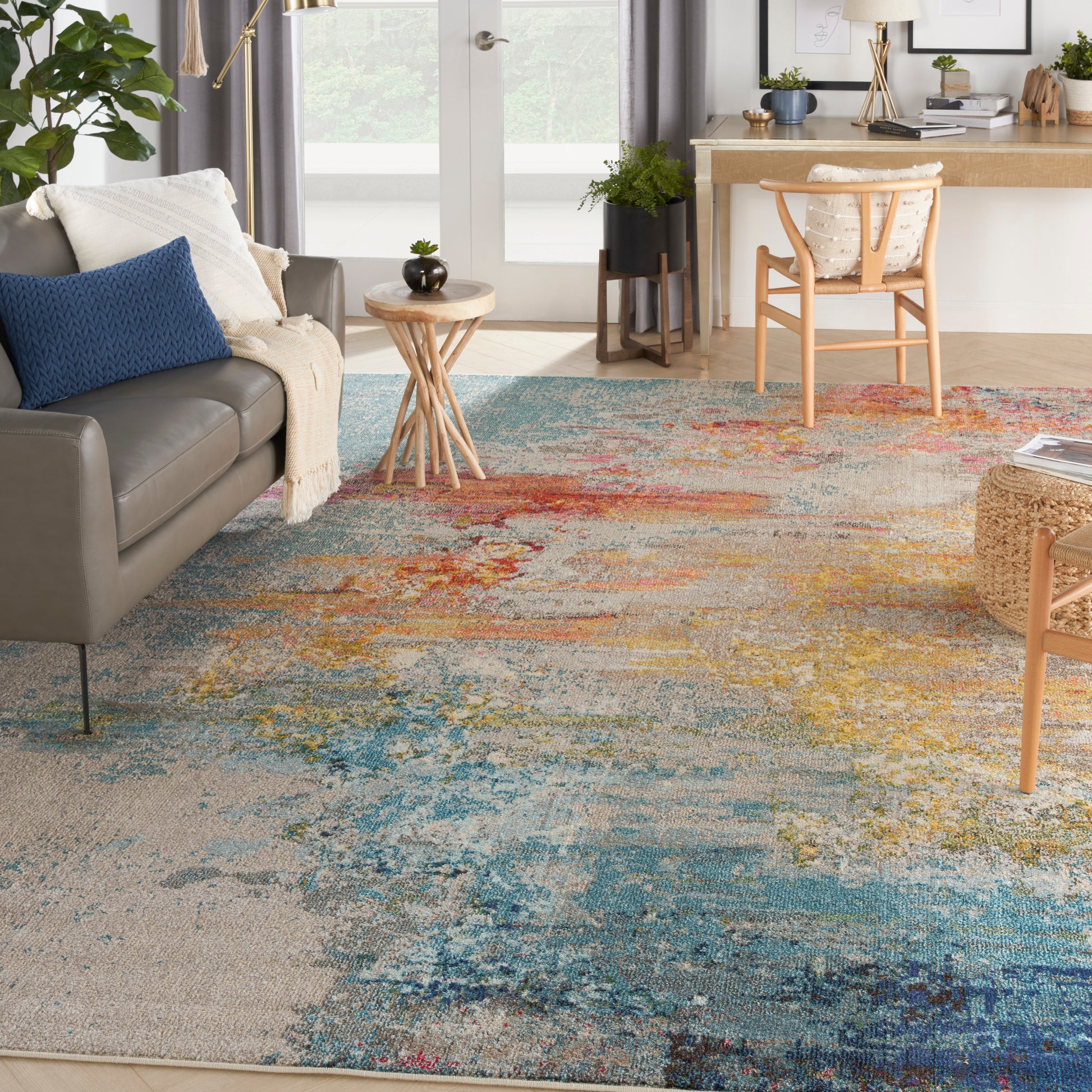 Cozy living room with vibrant multicolor rug, grey sofa with blue cushion, round wooden side table, light wood desk and chair