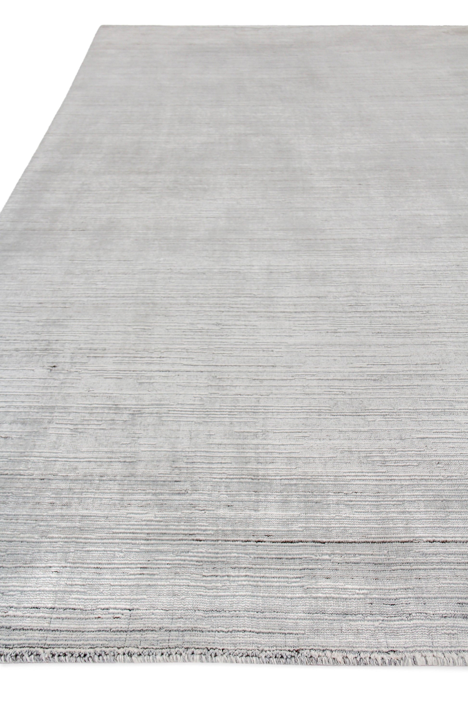 Light gray hand loomed indoor rug with subtle horizontal stripes & fringed edge for modern living spaces.