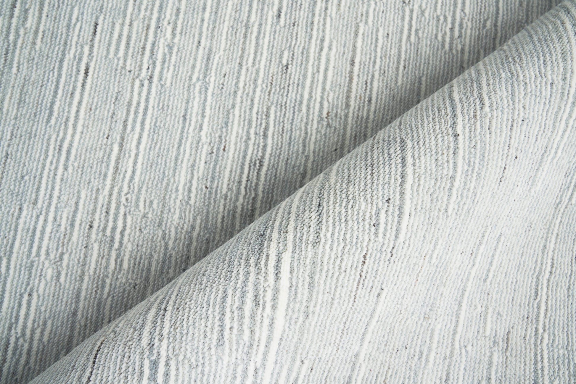 Light gray textured rug with thin vertical ridges, folded to show soft drape.