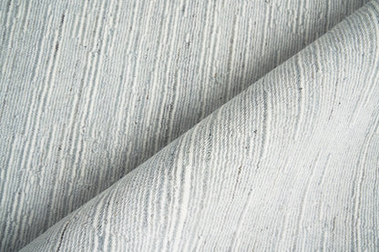 Light gray textured rug with thin vertical ridges, folded to show soft drape.