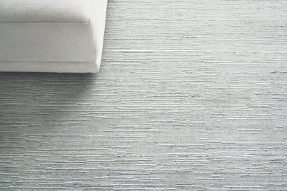 Light gray textured area rug with subtle horizontal stripes; beige sofa corner in a modern minimalist living room.