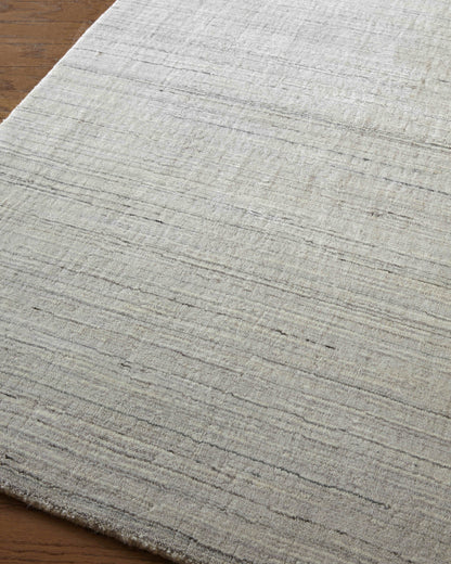 Light gray textured rug with subtle horizontal stripes and a fringed edge on a wood floor.