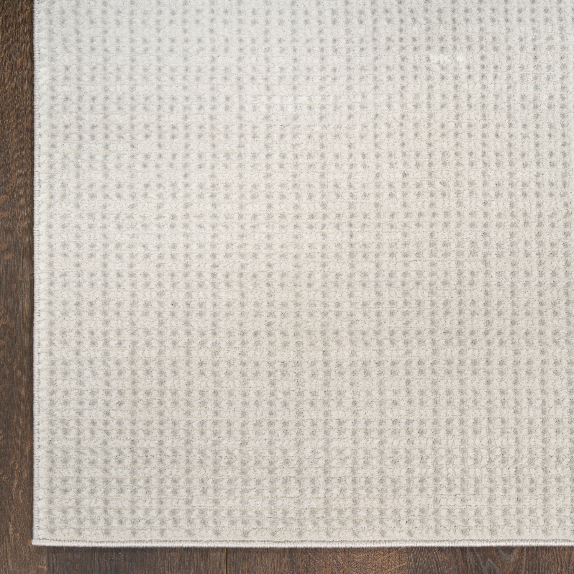 Beige textured woven fabric swatch with subtle grid pattern on a wooden floor.